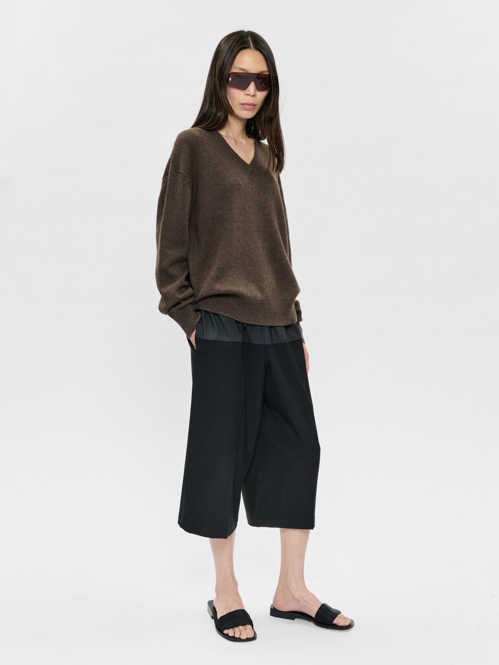 Woman wearing a brown sweater and black pants on a white background