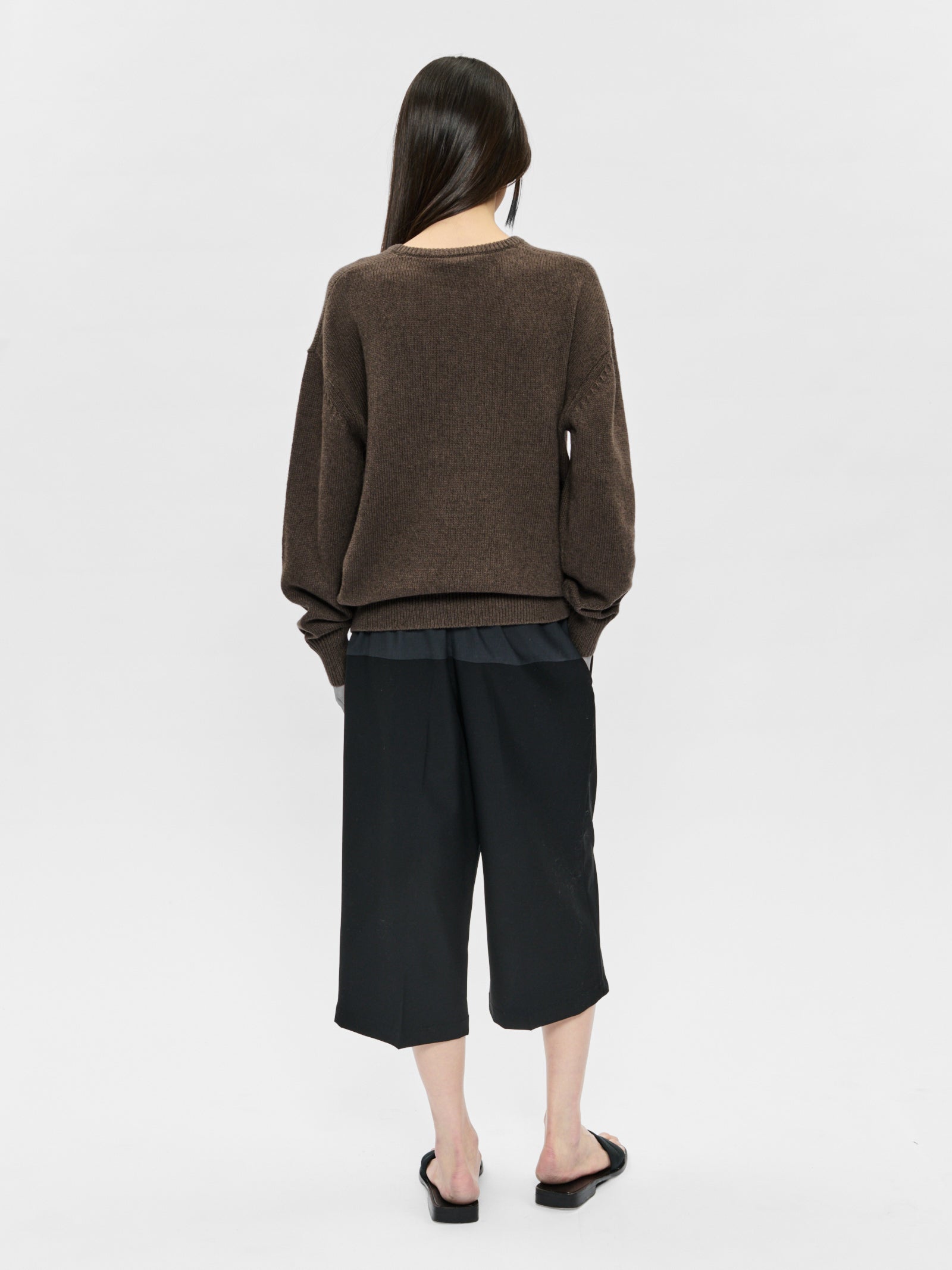 Person wearing a brown sweater and black pants on a white background