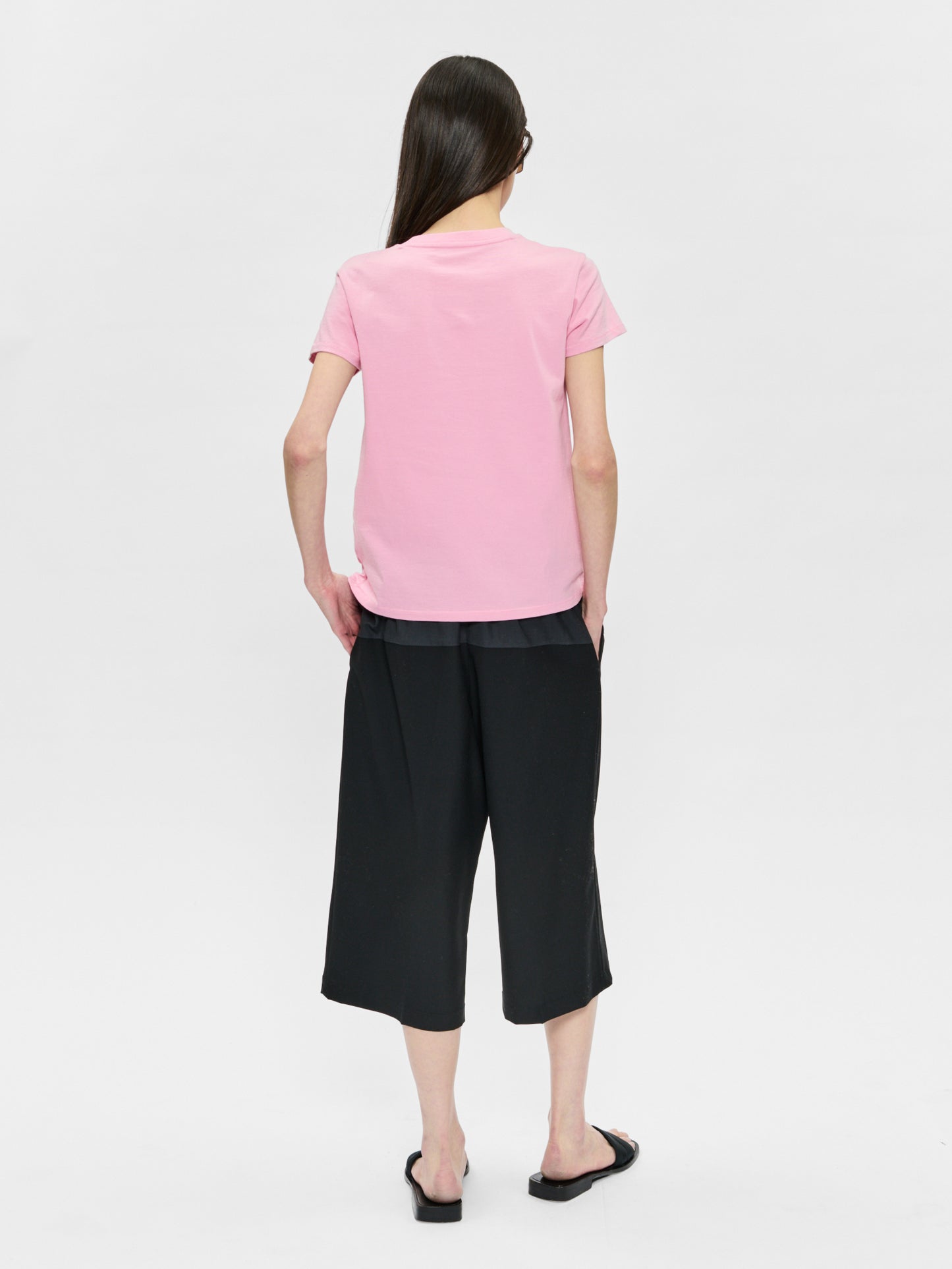 Person wearing a pink t-shirt and black pants on a white background