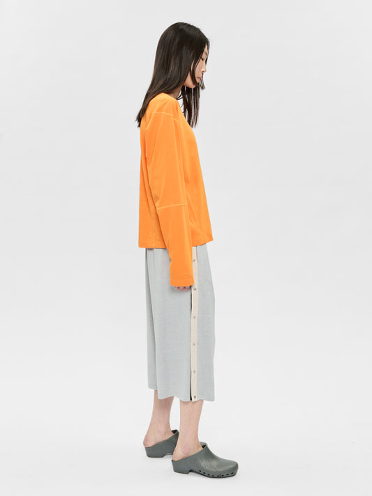 Woman wearing an orange sweater and gray pants on a white background