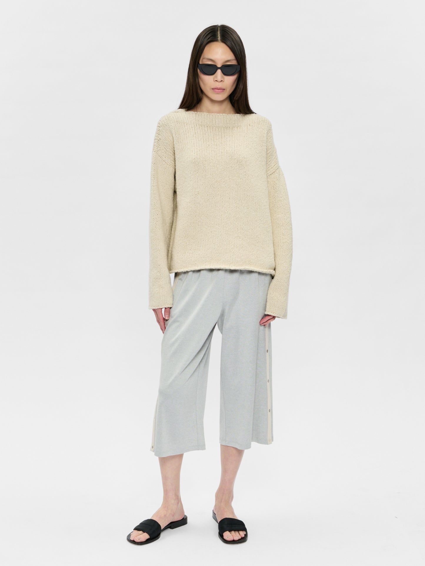 Woman wearing a beige sweater and light gray pants on a white background