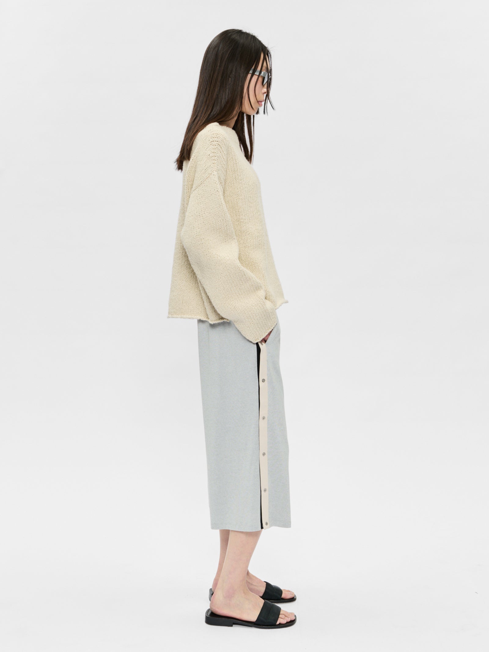 Woman wearing a beige sweater and light gray skirt on a white background