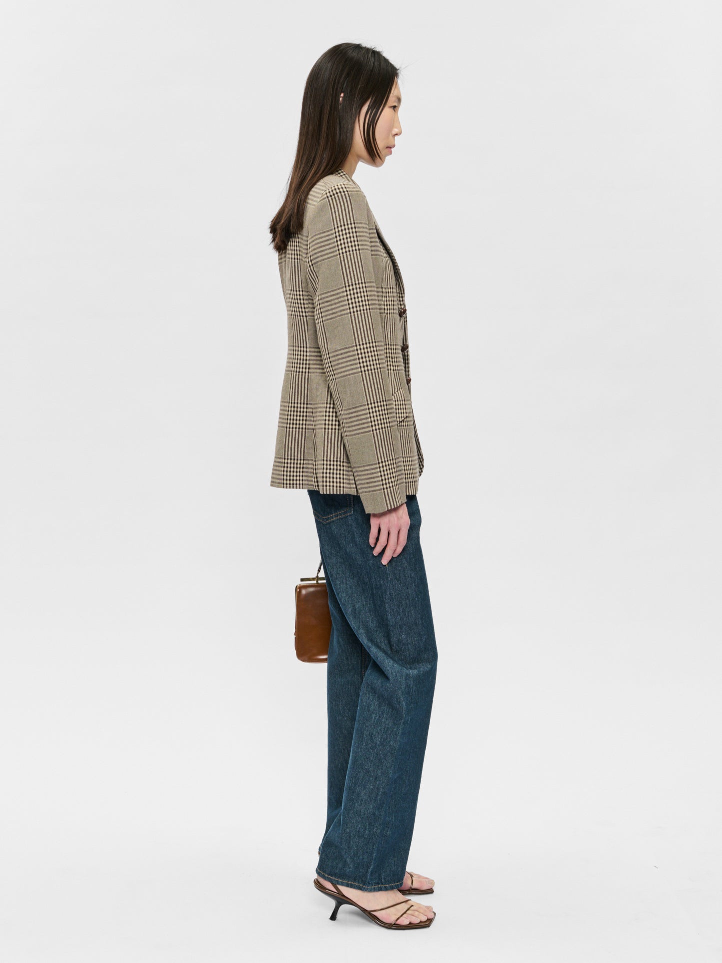 Woman wearing a checkered blazer and blue jeans on a white background