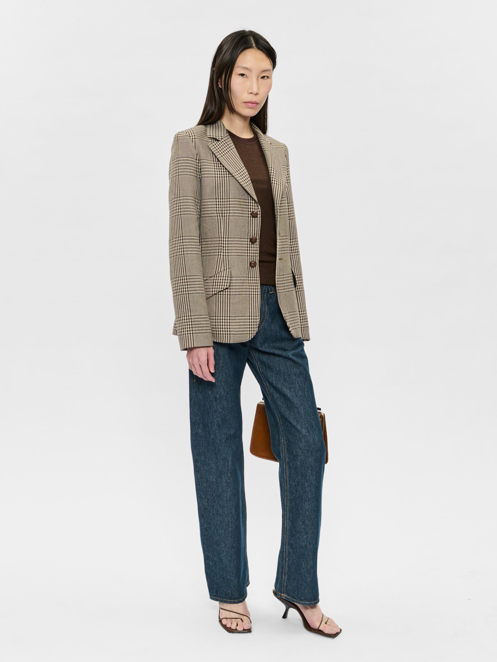 Woman wearing a checkered blazer and blue jeans on a white background