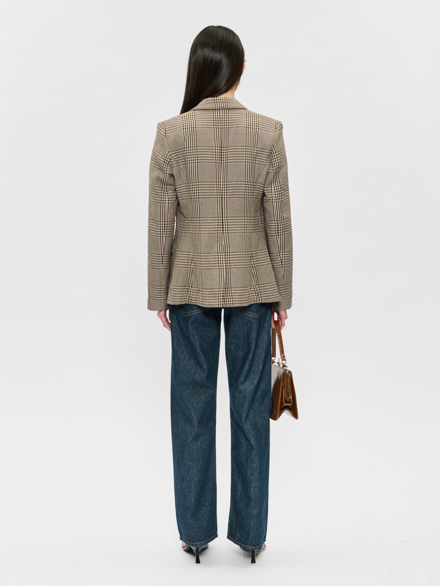 Person wearing a beige checkered blazer and blue jeans on a white background