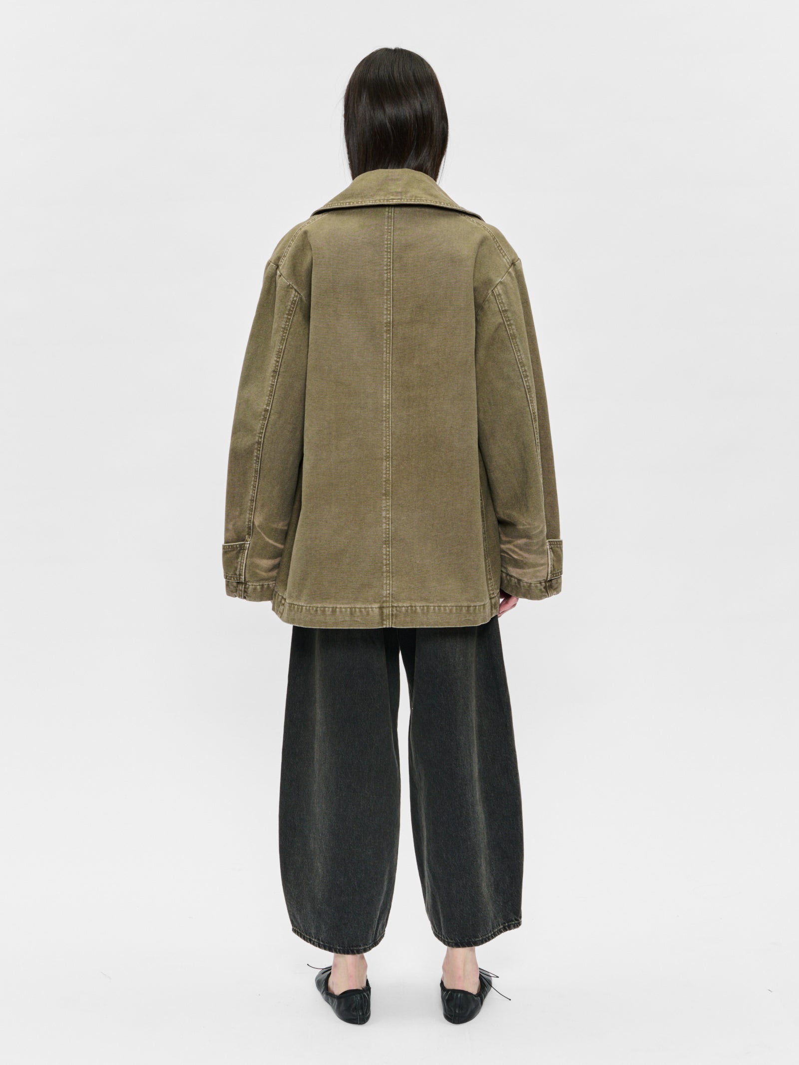 Person wearing a green jacket and black pants on a white background