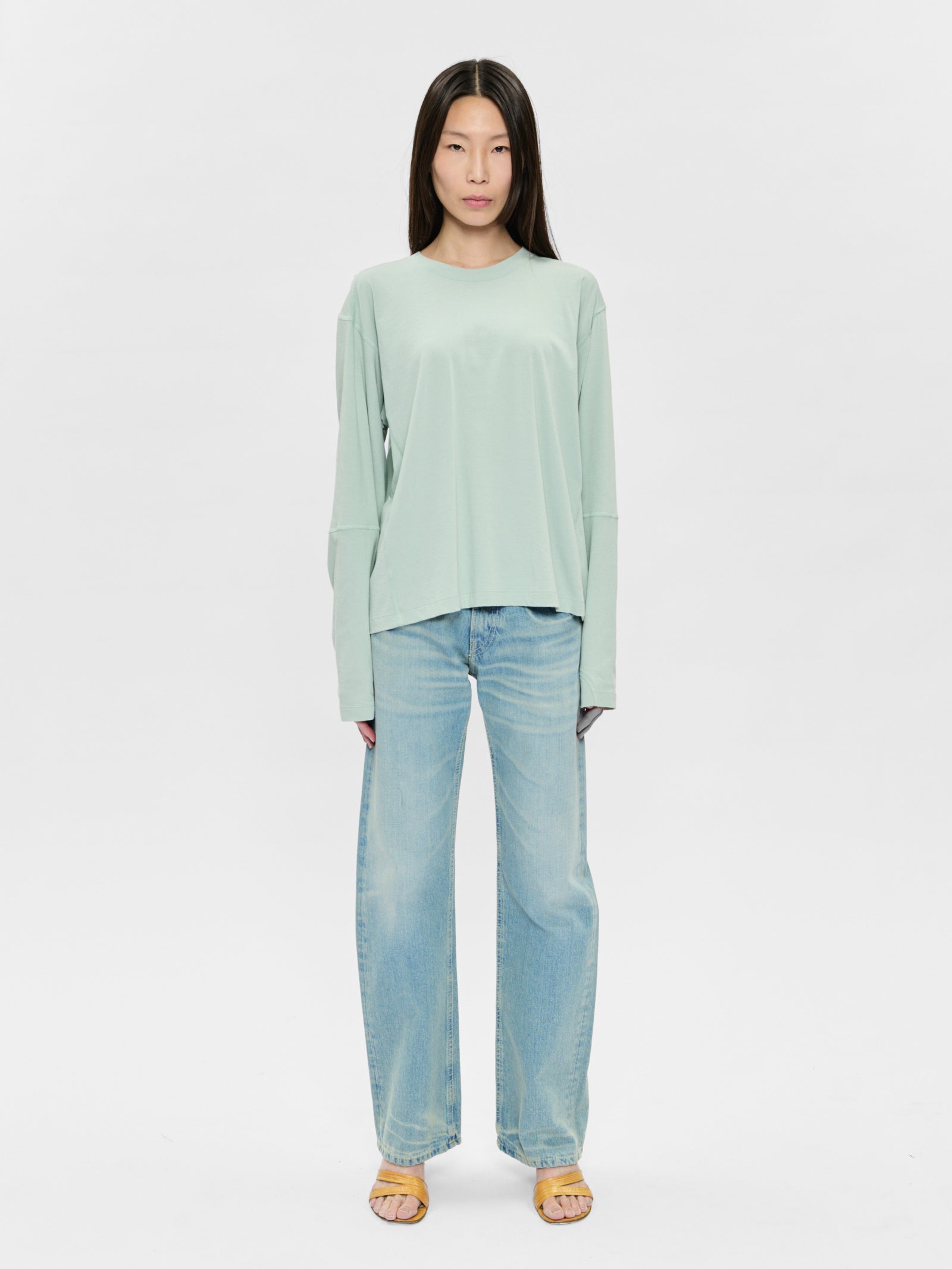 Woman wearing a light green top and blue jeans on a white background