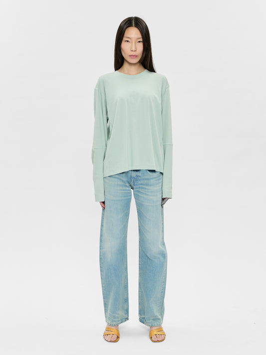 Woman wearing a light green top and blue jeans on a white background