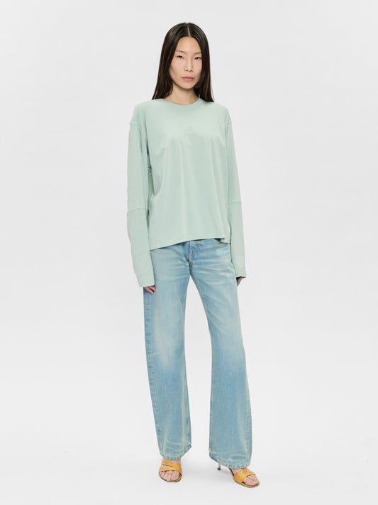 Woman wearing a light green sweater and blue jeans on a white background