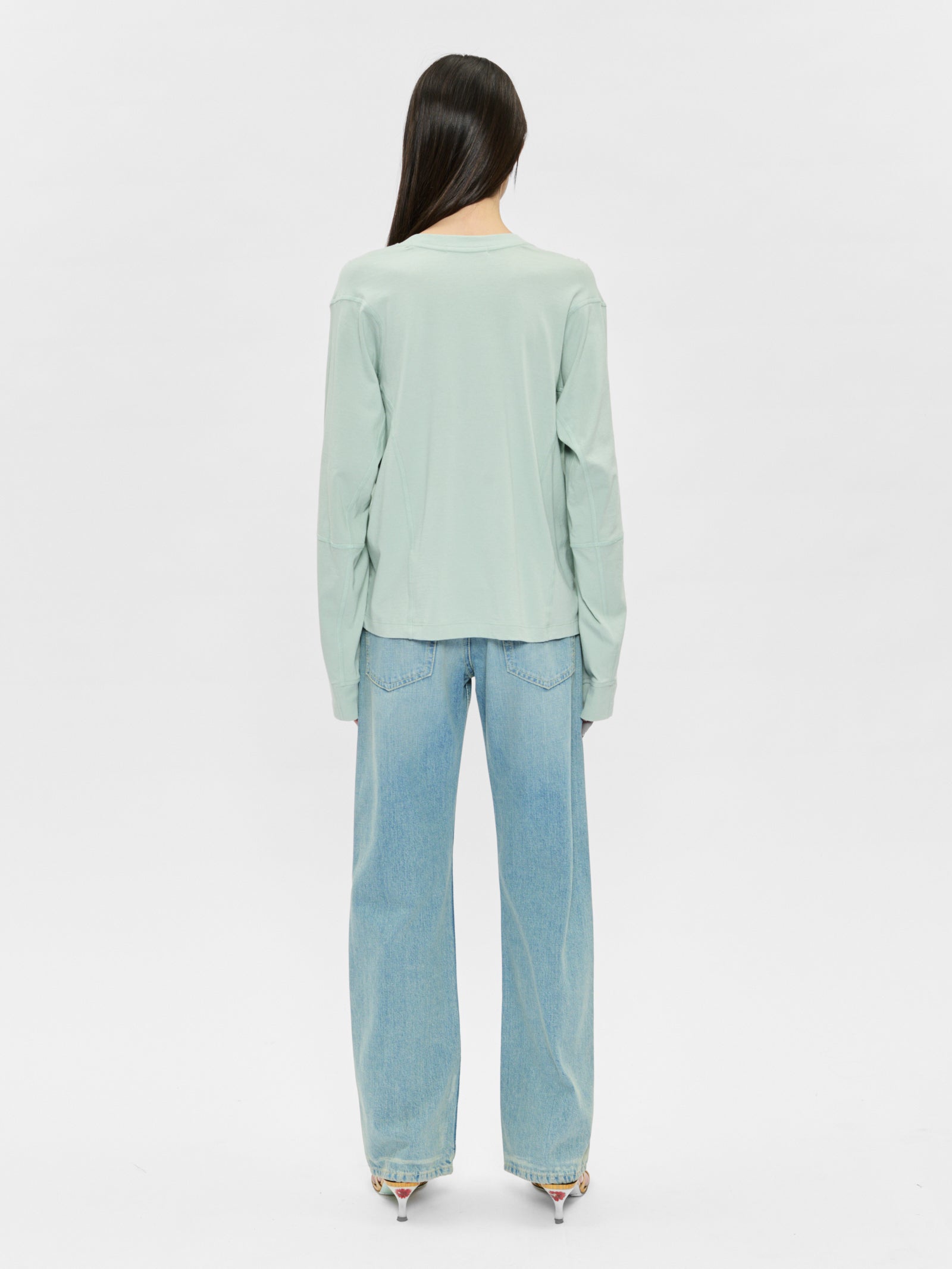 Person wearing a light green sweater and blue jeans on a white background